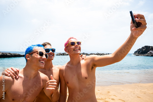 group of young people or teeager having fun and enjoying life and summertime together - happy millennials taking a selfie together at the beach on the sand with the sea or ocean at the background photo