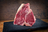 Rohes dry aged Wagyu Porterhouse Steak Block vom Rind angeboten als close-up auf einem schwarzen verkohlten Holz Board mit Textfreiraum