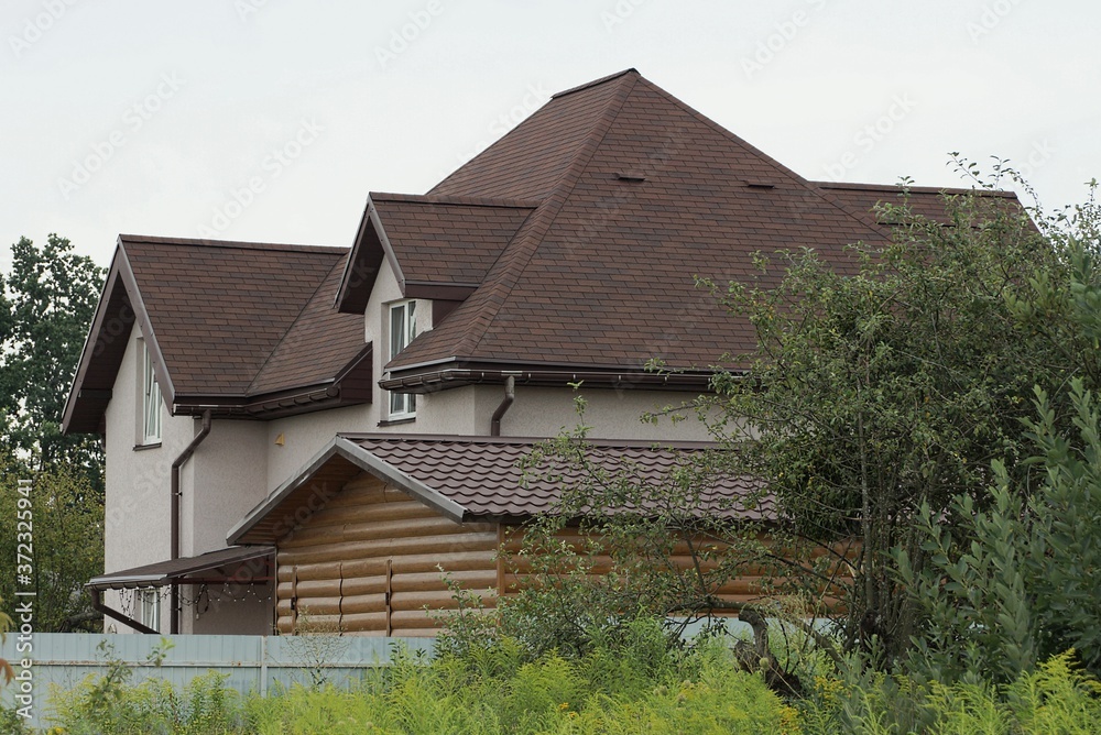 large gray private house with a brown tiled roof overgrown with green vegetation against the sky