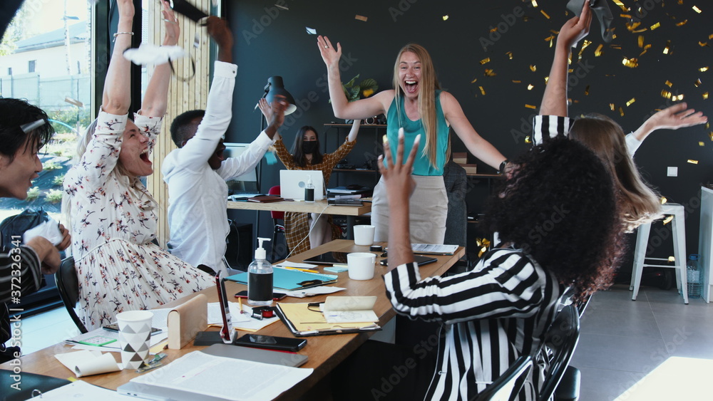 Obraz premium COVID-19 is over. Happy multiethnic business people team take masks off, celebrate normal life with confetti at office.