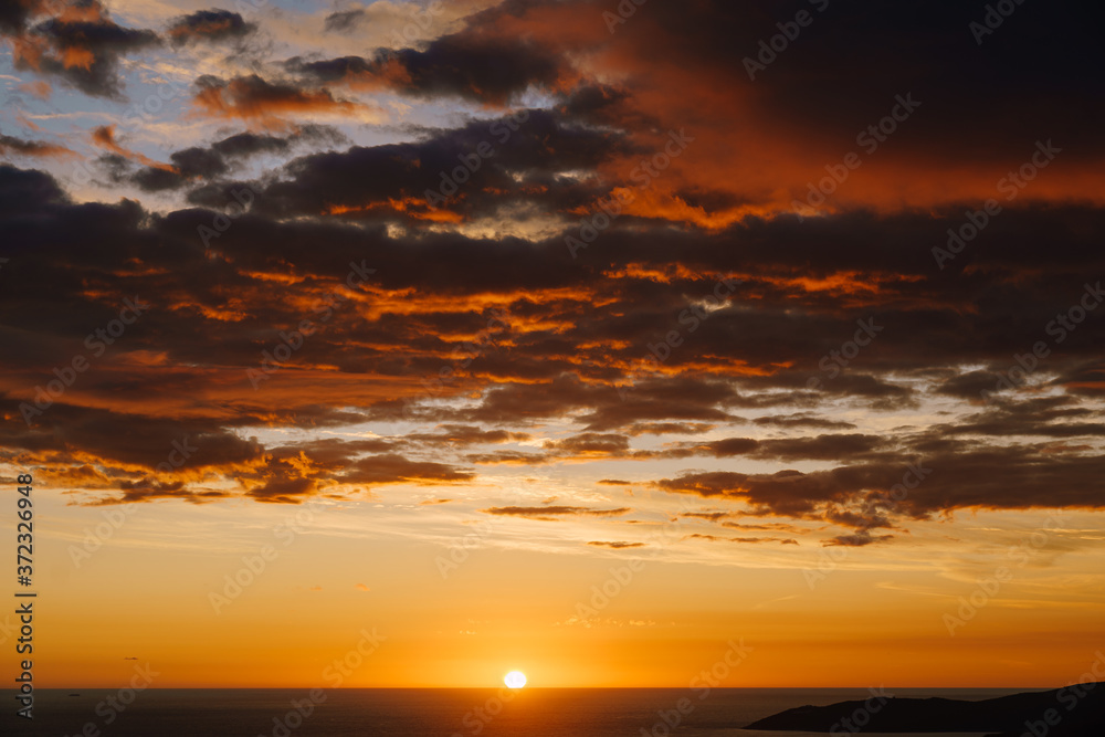 Fiery orange sunset over the sea. The sun sets behind the horizon, orange clouds in the sky.