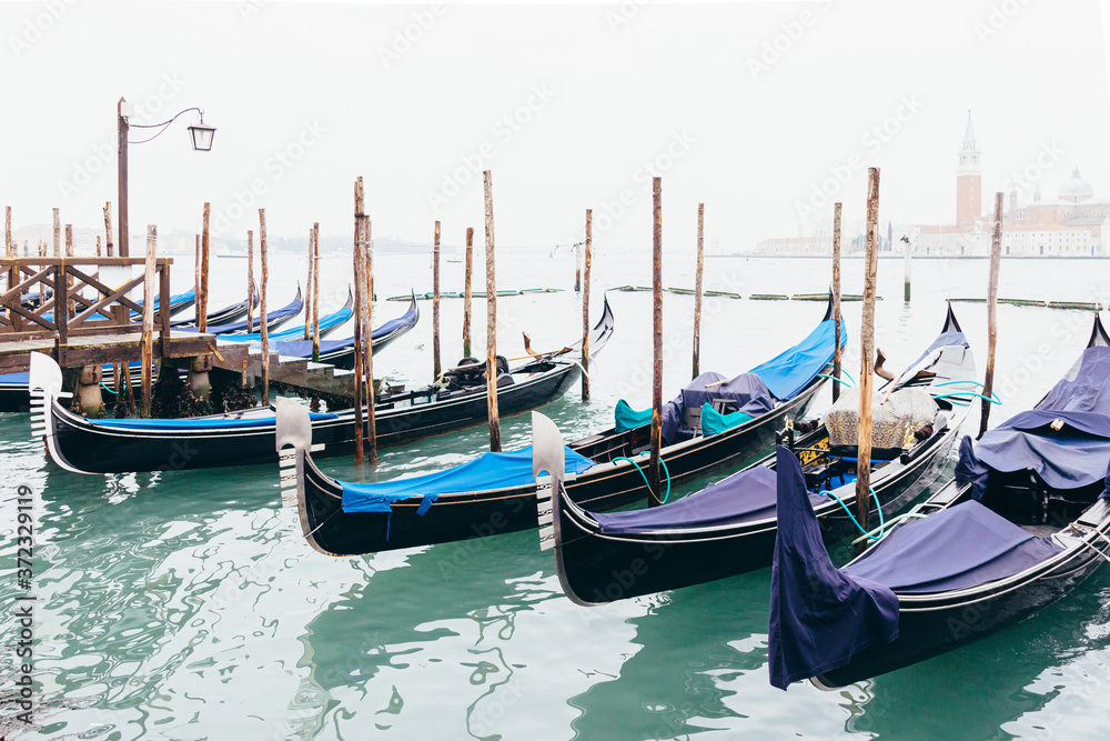 Gondolas moored on the Lagoon, San Giorgio Maggiore beyond, Riva degli Schiavoni, Venice, Veneto. On a cloudy day with fog.