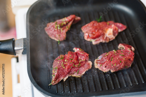 Four raw steaks are fried on a grilled pan.