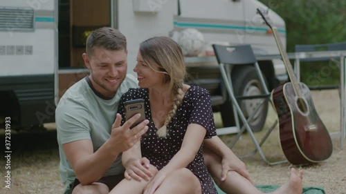 Young family couple talking video calling against motor home RV campervan. Man and woman enjoyng vacation in road trip.
 photo