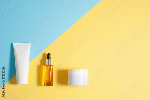 Cosmetic skin care yellow oil and white jars with creme on the colorful blue and yellow background flat lay top view