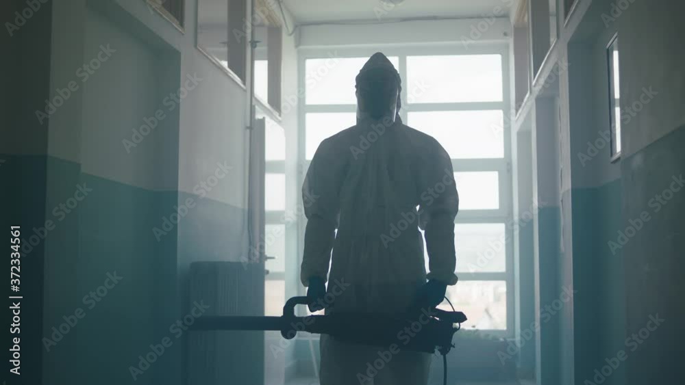 This video shows a man in protective overalls sanitizing a school corridor, spraying a disinfectant solution all over the passage. This video shows a man in protective overalls sanitizing a school corridor, spraying a disinfectant solution all over the passage.