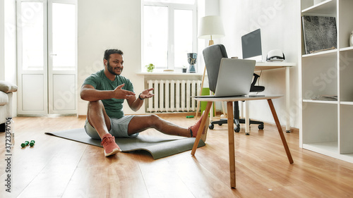 Motivate. Male fitness instructor explaining exercises while streaming, broadcasting video lesson on training at home using laptop. Sport, online gym concept