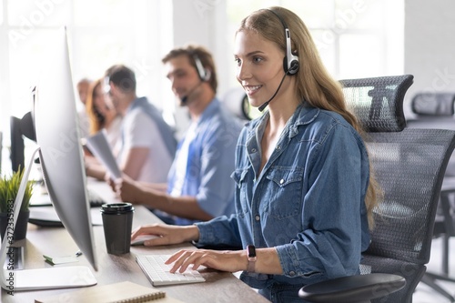 How can I help you? Beautiful call center workers in headphones are working at modern office.