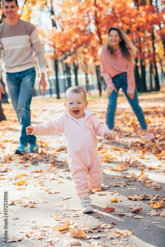 little kid girl runs in autumnal couple and plays with parents. toddler runs away on autumn yellow leaves from mother with father