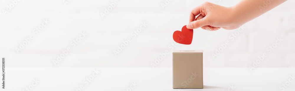 cropped view of female hand putting red heart in box on white background, donation concept - obrazy, fototapety, plakaty 