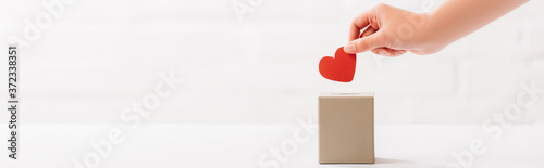 Vászonkép cropped view of female hand putting red heart in box on white background, donati