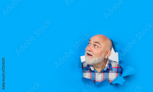 Advertising. Smiling bearded man making hole in paper. Insert text or slogan. Man through paper. Copy space for advertising. Bearded man looking through hole in paper. Discount. Sale.