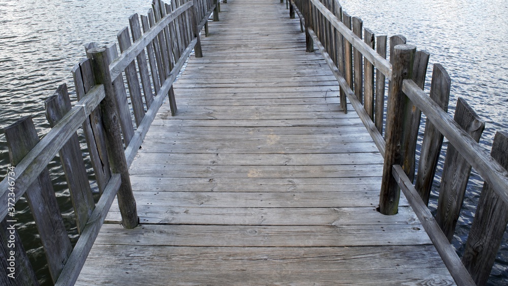 A wooden pier with handrails leading to an artificial island in the middle of the lake. A wooden pier with handrails leading to an artificial island in the middle of the lake.