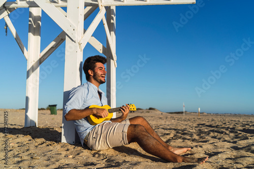 Hombre joven alegre cantando con un Ukelele en la playa