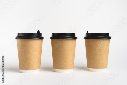 Three eco friendly paper craft cups for coffee to go with black lid on the white background. Zero waste, plastic free concept. Sustainable lifestyle. Composition with front view.