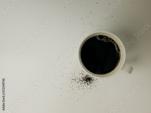 Top down view of white coffee mug with coffee grounds spilled around the cup on a white countertop