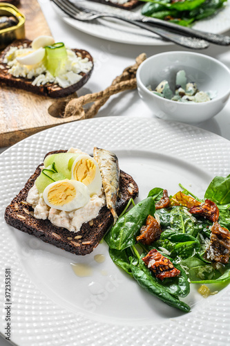 Delicious appetizer tapas, soft boiled eggs and canned sardines sandwiches. Salad with spinach and dried tomatoes. White background. Top view
