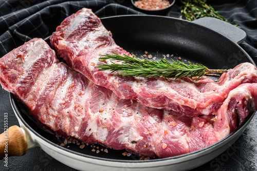 Raw pork spare ribs with spices and herbs in a pan. Black background. Top view