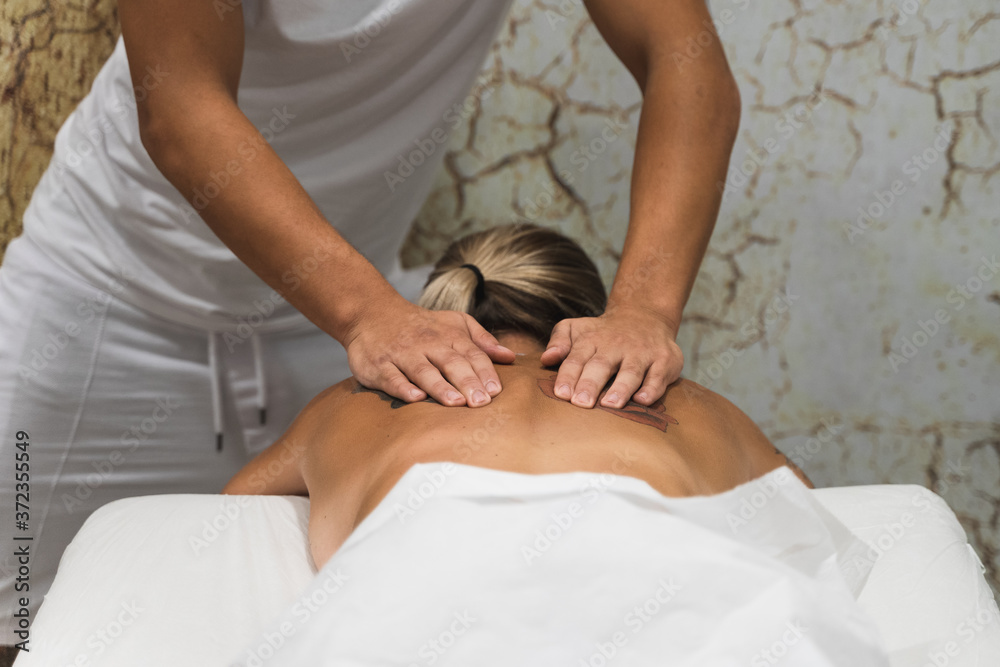 Palma, Majorca, Spain - August 10, 2020: Hands of a masseur applying chiromassage treatment on the back of a young woman with tattoos