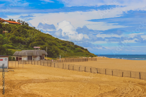 Ocean beach with yellow sand and mountains, with a wooden fence. Blue sea with foam, sunny day, blue sky.