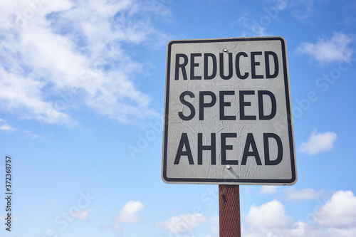 Fényképezés Reduced speed ahead sign against blue sky and clouds