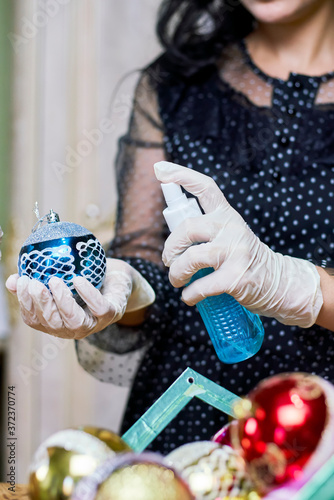 Disinfecting festive toys. Woman pour antiseptic spray to Xmas ball. Woman in medical gloves prepare Christmas decoration