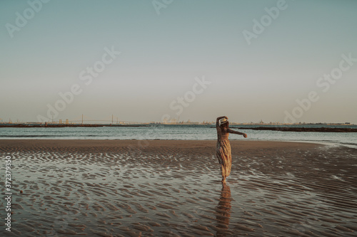 Chica joven y guapa con vestido y sombrero paseando por la playa
