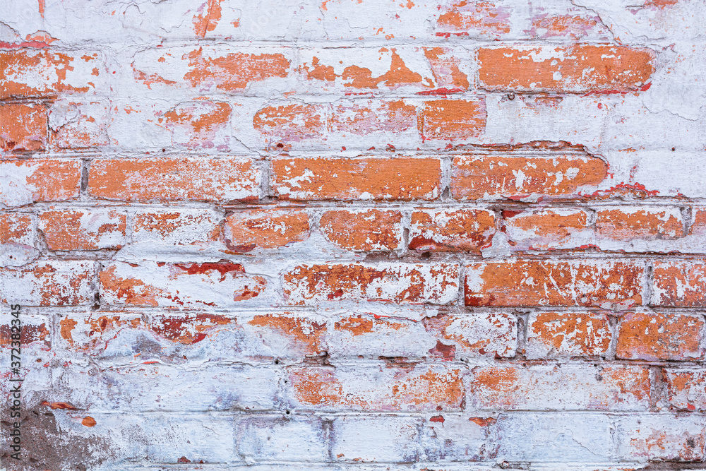 Fototapeta premium Old, antique wall of red destroyed bricks. White plaster was applied to the top of the brickwork. The plaster has peeled off significantly.
