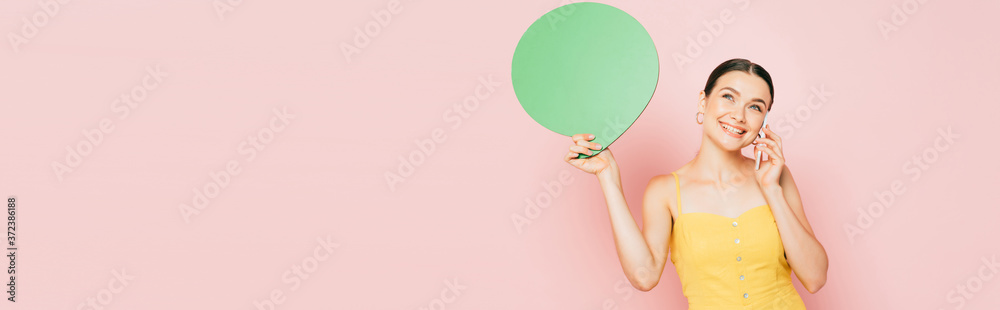 brunette young woman with green blank speech bubble talking on smartphone on pink, panoramic shot brunette young woman with green blank speech bubble talking on smartphone on pink, panoramic shot