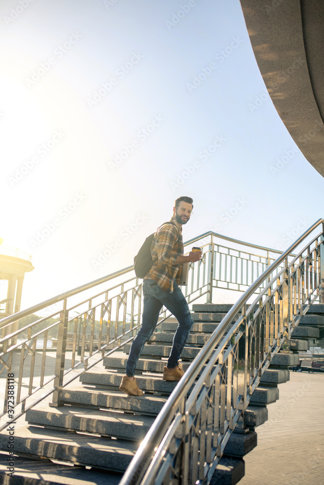 Joyful man with backpack and coffee climbing stairs