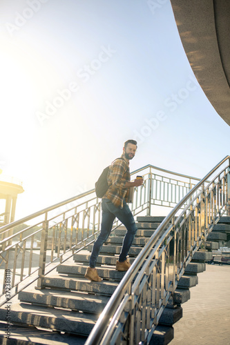 Joyful man with backpack and coffee climbing stairs
