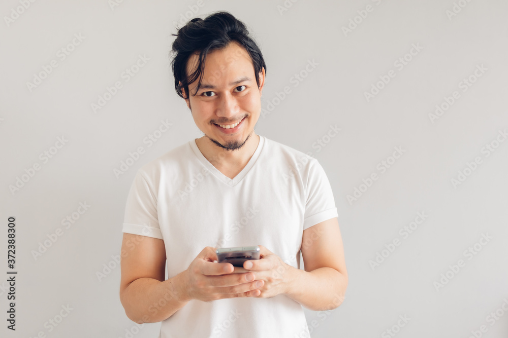 Happy long hair Asian man in white casual t-shirt is using smartphone. Happy long hair Asian man in white casual t-shirt is using smartphone.