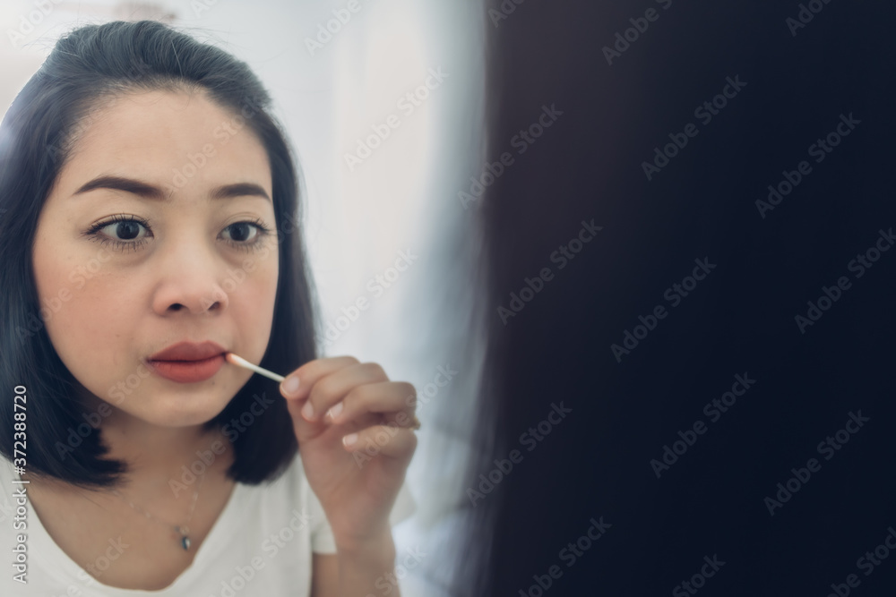 Asian woman is checking her lips on the mirror in white room. Asian woman is checking her lips on the mirror in white room.