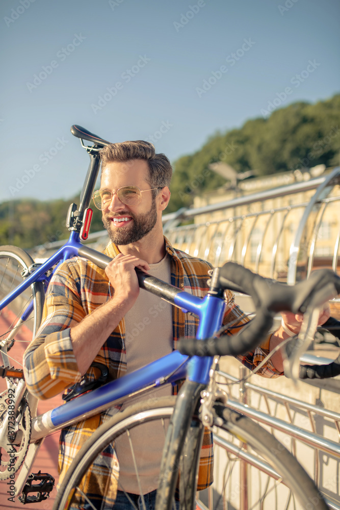 Naklejka premium Man standing on street holding bicycle on his shoulder