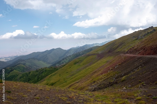 Beautiful view of green mountains with dangerous gravel road. Ketmen or Ketpen mountains gorge and mountain pass. Tourism in Kazakhstan.