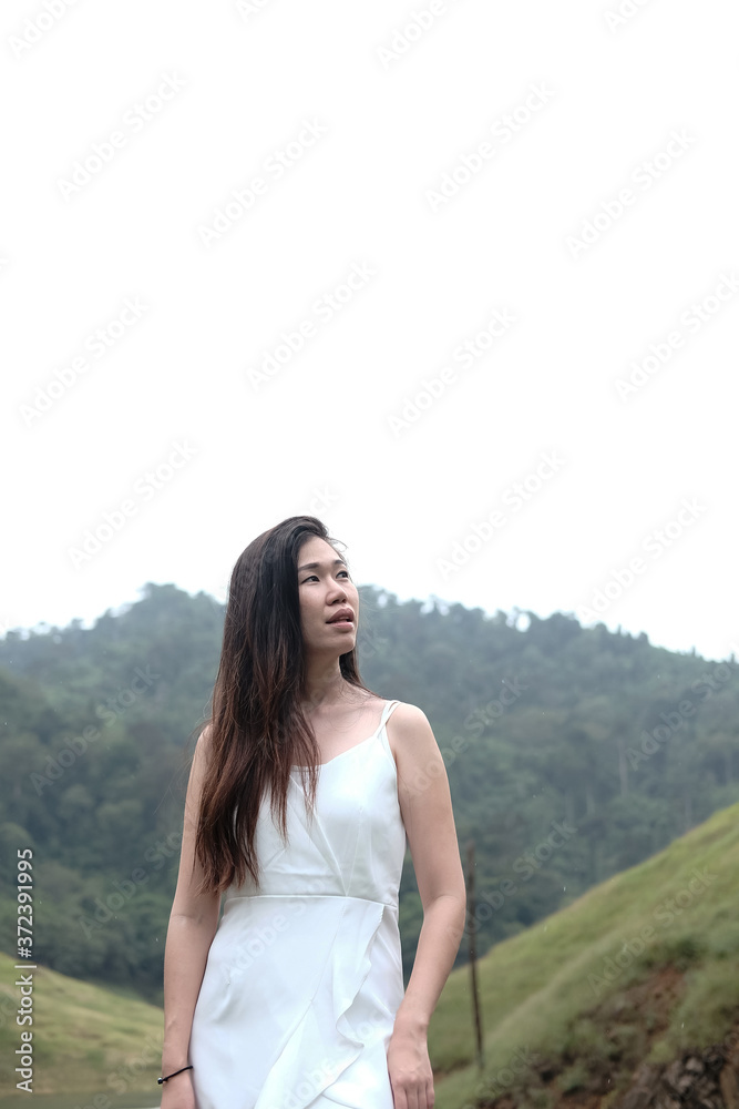 Smiling beautiful young Asian girl wear white dress standing on grass meadow beside the stream in tropical rainforest. Smiling beautiful young Asian girl wear white dress standing on grass meadow beside the stream in tropical rainforest.