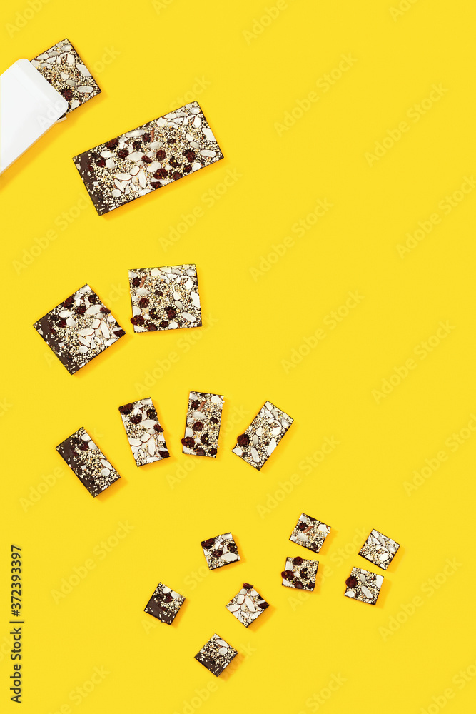 Bitten bar of chocolate is broken into several pieces, chocolate with nuts and dried fruits on yellow background Bitten bar of chocolate is broken into several pieces, chocolate with nuts and dried fruits on yellow background