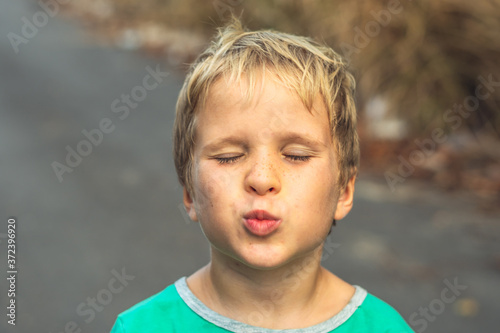 Funny mischievous cute blond boy making freckles face showing love kiss, artistic emotions gesturing. Family relationship, micro moments joys of happy childhood, compassion toward humanity and society