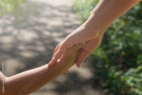 Mother and child hold hands on a walk in the park. © Elena Shi