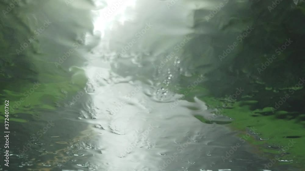Abstract designs created by rain drops and droplets falling and splashing on car windshield as it travels on wet asphalt rural countryside road on rainy dreary day, handheld close up slow motion Abstract designs created by rain drops and droplets falling and splashing on car windshield as it travels on wet asphalt rural countryside road on rainy dreary day, handheld close up slow motion