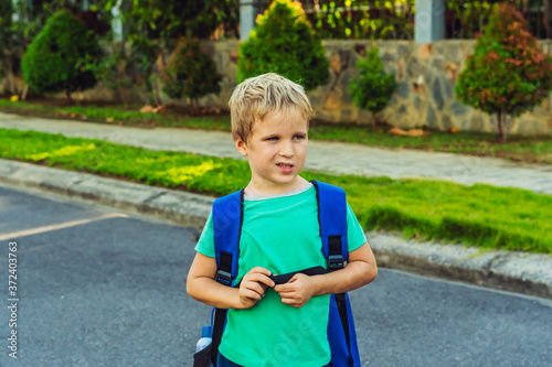 Billede på lærred Funny mischievous cute blond boy with freckles blue backpack from school or kindergarten, artistic emotions facial expression