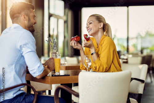 Cheerful woman eating donut and talking to her boyfriend in a cafe.