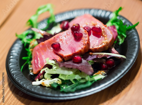 Raw tuna slices seasoned with mustard sauce on black dish with frisee leaves and pomegranate grains