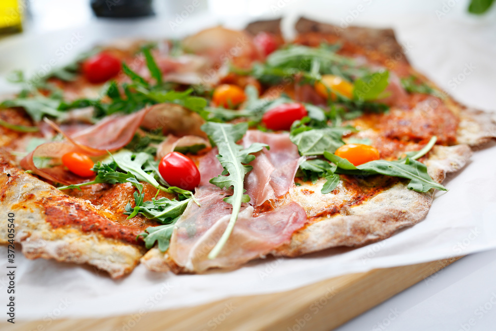 The cook is preparing a delicious pizza. Traditional Italian pizza with Parma ham, cherry tomatoes and arugula. The cook is preparing a delicious pizza. Traditional Italian pizza with Parma ham, cherry tomatoes and arugula.
