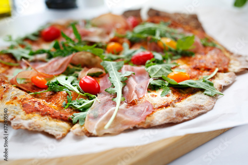 The cook is preparing a delicious pizza. Traditional Italian pizza with Parma ham, cherry tomatoes and arugula.