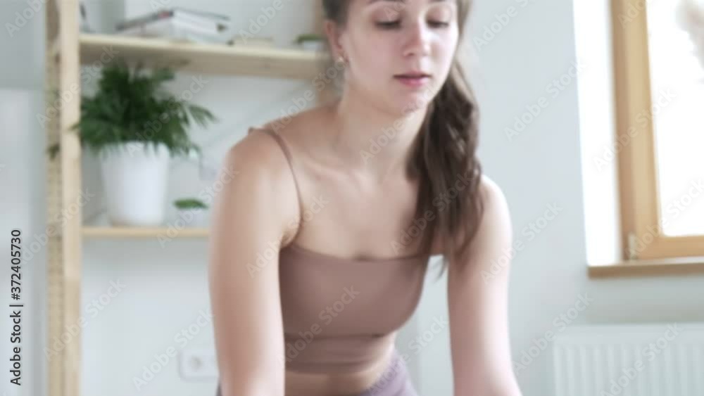 Young brunette girl with ponytail in sportswear in bright room. sporty sexy caucasian female standing on knees, lifting head up. sports, fitness training at home. Healthy lifestyle, leisure, activity