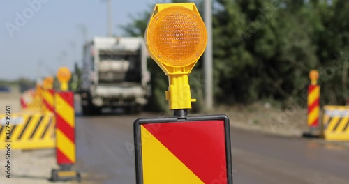 Shallow depth of field footage with road warning lights on a construction site and a garbage truck passing by.