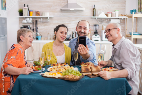 Family smiling on video call while having lunch in kitchen. Wife with husband   mother and father during a call during brunch.