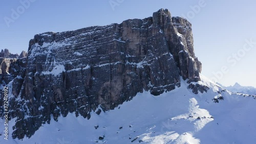 Breathtaking bird's eye view of majestic high mountains covered with snow under blue sky.Camera flying over scenery rock cliff, picturesque aerial view of beautiful nature landscape of Alps in winter
