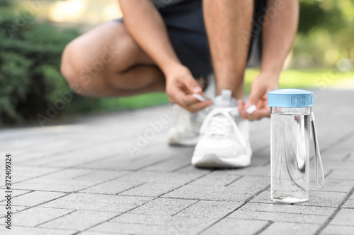 Bottle of water and sporty man tying shoelaces in park